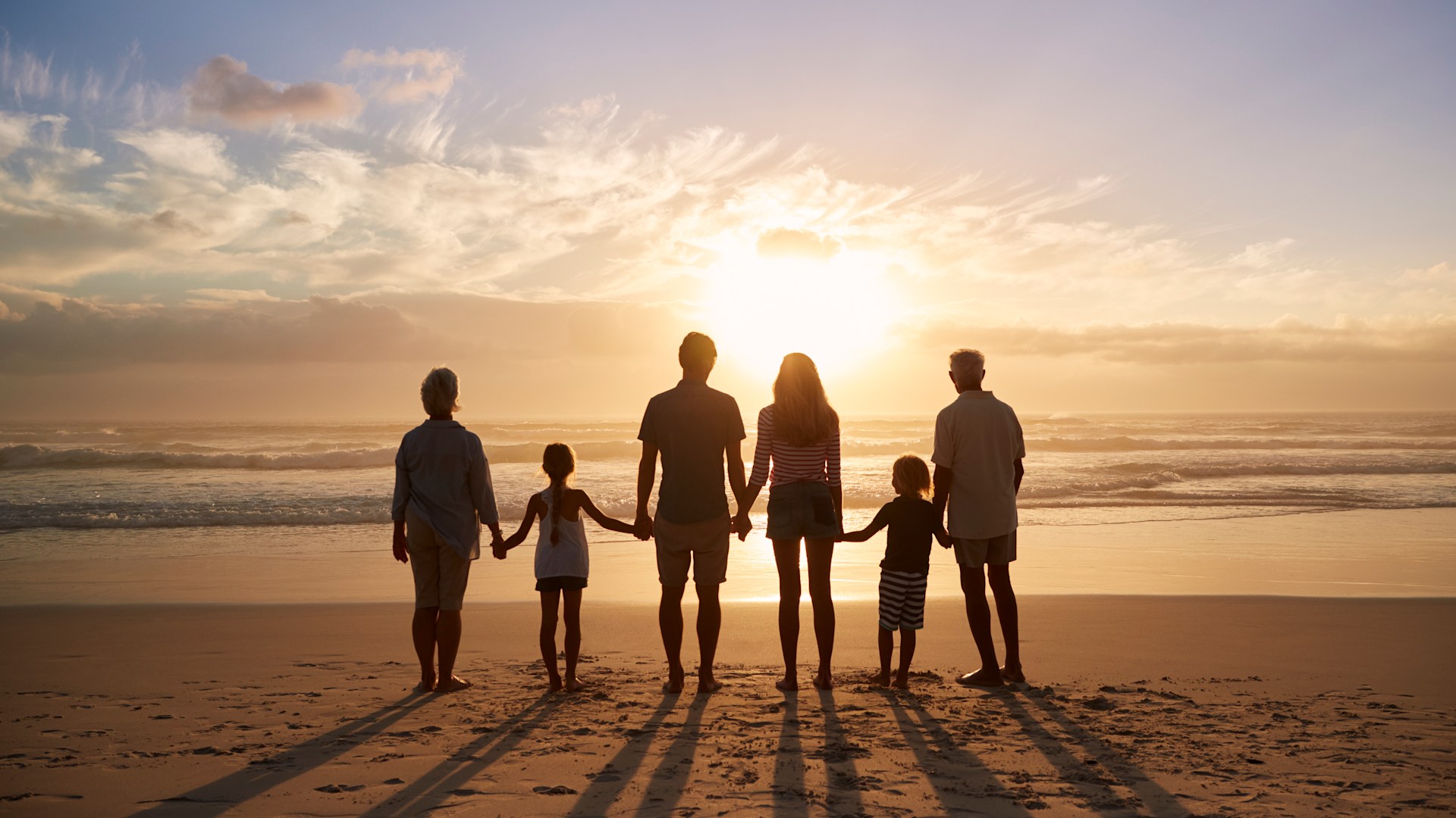 Family of four walking along a sunny beach, holding hands and enjoying quality time together during a fun seaside vacation.