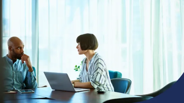 Two female colleagues discuss work during a professional meeting with a laptop on the table.