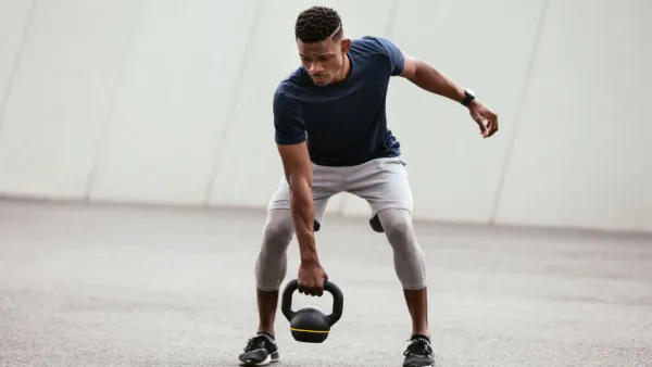Man performing a kettlebell exercise during an outdoor strength training workout to build muscle, improve balance, and boost overall fitness.