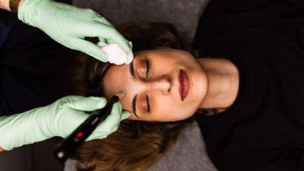 A woman receives a cosmetic facial treatment as a practitioner uses a handheld device on her forehead.