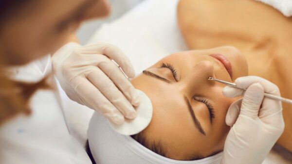A skincare professional performs blackhead extraction on a woman’s face using a comedone removal tool.