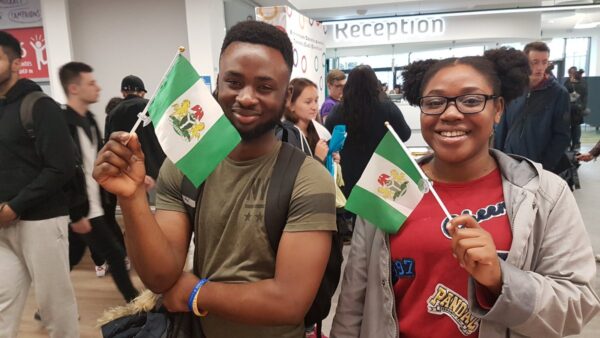 wo Nigerian travellers holding Nigerian flags inside an airport terminal.