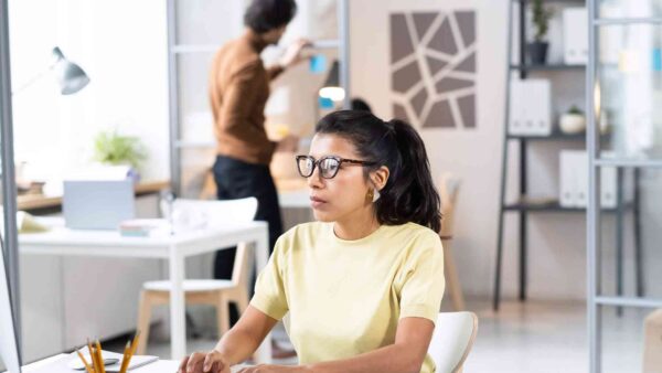 Woman wearing glasses working at a computer in a modern office.