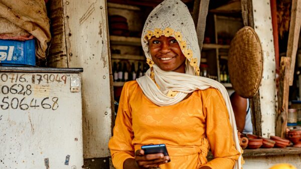 A woman standing in front of a fruit stand holding a mobile phone