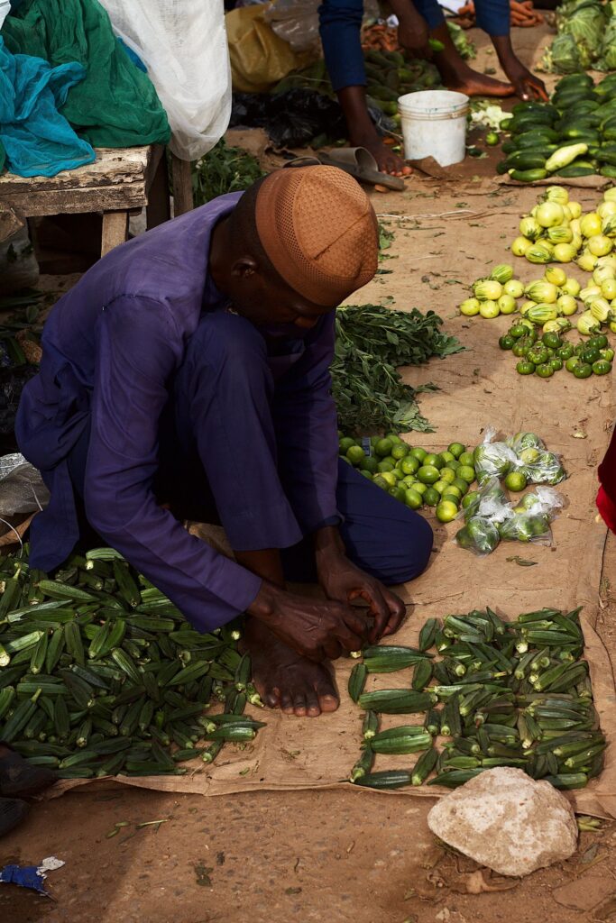 A market vendor arranging fresh okra and vegetables at a stall in Kaduna