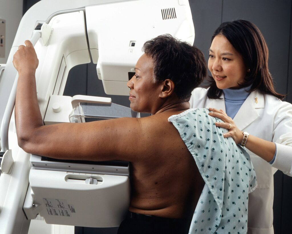 A technician positioning a woman at a mammogram machine for breast cancer screening