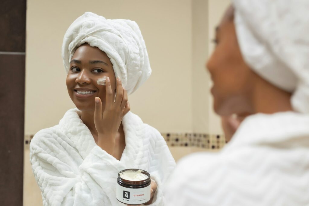 A woman with a towel on her head applying cream to her face